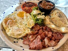 Delicious english breakfast with fried eggs, bacon, bread and vegetables photo