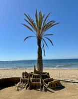 Sandcastle on a beach with palm trees and blue sky on a sunny summer day photo