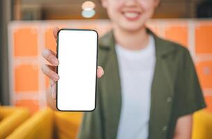 Smiling young asian woman using mobile phone checking social media,app playing game, shopping online, ordering delivery relax while sitting on a couch at cafe with laptop computer photo