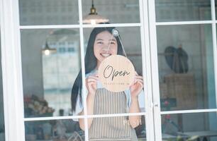 Smiling online small business owner holding a sign saying Open and happily working at a courier business offering orders and products to customers.Online retailer - online shopping. photo