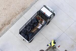 Aerial view of a Electric vehicle loaded with garbage bags and a street cleaner working to collect trash in a city beach area photo
