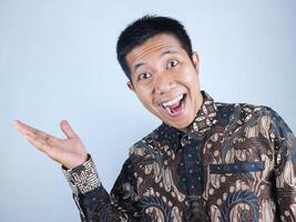 Smiling expression of asian man wearing batik clothes presenting copy space or showing something photo