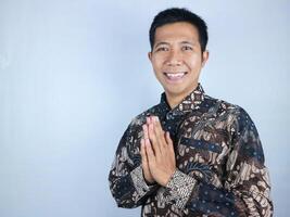 Smiling face ecpression of asian man wearing batik clothes looking at the camera doing greeting pose photo
