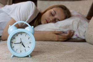 Alarm clock on sofa will soon wake up the young caucasian girl in the background who is lying on pillow during nap, control of human sleep photo