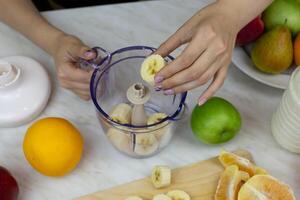 Women hands put banana pieces in container for grinding with blender, making tonic drink from fruits at home, simple recipe for healthy drink with vitamins photo