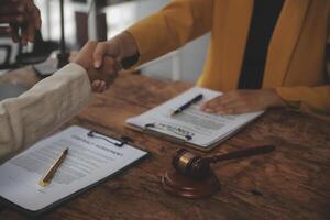 Lawyer shaking hands with a client making about documents, contracts, agreements, cooperation agreements with a female client at the lawyer's desk and a hammer at the table. photo