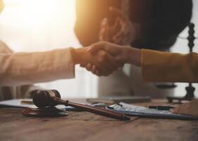 Lawyer shaking hands with a client making about documents, contracts, agreements, cooperation agreements with a female client at the lawyer's desk and a hammer at the table. photo
