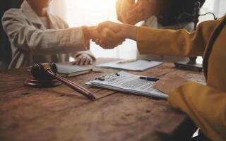 Lawyer shaking hands with a client making about documents, contracts, agreements, cooperation agreements with a female client at the lawyer's desk and a hammer at the table. photo