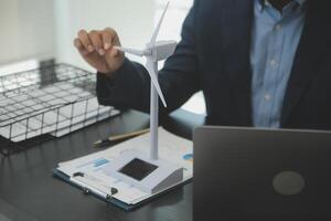 Shut of handsome business man working on new alternative energy development looking at a model of a wind turbine in modern startup. photo