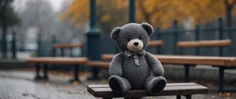 Black and white Lost teddy bear sitting on bench at playground in gloomy day. photo
