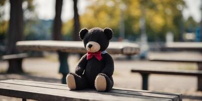 Black and white Lost teddy bear sitting on bench at playground in sunny day. photo