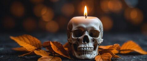 A candle with a skull on it is lit in front of a bunch of orange leaves. photo