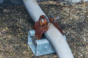 Rusty metal clamp holding electrical conduit on rooftop. photo
