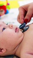Pediatrician hand puts stethoscope on child's chest. Baby looks interested and smiles to the doctor. Blurred backdrop. Vertical video
