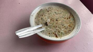 Indonesian Soup with Meat and Spices Coto makasar. Close-up view of a bowl of Indonesian soup, containing meat and various spices. The soup is in a white bowl on a pink table. photo