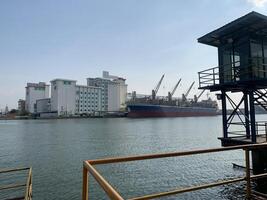 Cargo Ship Docked at a Port. A large cargo ship docked at a port, with several industrial buildings and cranes in the background. photo