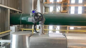 Industrial Valve and Piping System in a Manufacturing Facility. A close-up of an industrial valve and piping system inside a manufacturing facility. The valve is attached to a green pipe. photo
