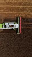 Harvester machine cuts the crop of dry wheat. Thick smoke and dust comes out from the combine. Aerial view. Vertical video