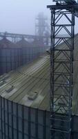 Metal tanks and constructions at modern grain processing plant. Foggy winter weather backdrop. Aerial view. Vertical video