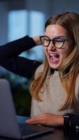 Woman sitting at computer, working on it and gets angry about something. Office employee screaming and waving hands in front of laptop. Vertical video