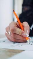 Process of drawing a sketch of a model dress on paper by female tailor. Professional designer draws with a pencil on the table in atelier. Vertical video