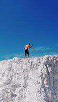 Drone view on the high white mountain and muscular man on top of it in summer. Topless young sportsman showing his trained body while standing on the top of the hill under blue sky. Vertical video