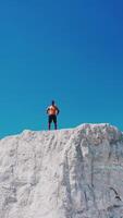 Drone view on a sportive man standing on the edge of the mountain. Shirtless athlete on the top of white canyon under clear sky in summer day. Vertical video