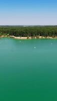 Smooth turquoise surface of water in former quarry. Drone footage over the lake and forest around it. Circle movement. Vertical video