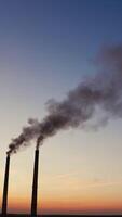 Pollution of the environment.Toxic smoke going from two pipes of a factory on the evening sky background at sunset. Vertical video