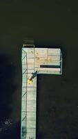 Top view of an active boy going into the edge of the bridge and jumping into the water. Little kid enjoys jumping and swimming in the river outdoors. Aerial view Vertical video
