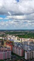 Urban background under beautiful sky. Modern city with high-rise buildings on green fields background. Aerial view. Camera rising up. Vertical video