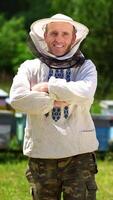 Beekeeper on a farm. Half-length portrait of male apiarist in a protective hat on the background of apiary. Production of natural product. Apiary concept. Vertical video