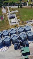 Grain elevators on field. Silver silos on plant for processing agricultural products. View from above on a modern granary for storing harvest. Aerial view. Vertical video