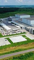 buitenkant van modern fabriek in landelijk plaats. vernieuwend complex met auto parkeren Aan groen natuur achtergrond. industrieel zone Aan velden. antenne visie. verticaal video