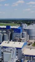 Grain elevators on nature background. Granary on a modern territory. Exterior of industrial factory with steel containers for grains. Vertical video