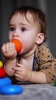 Cute toddler boy lying on the floor with toy pyramid. Lovely child took a toy top and put it into mouth. Blurred backdrop. Vertical video