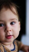 Cutest baby boy walks up closer to camera holding by the window sill. Lovely child learns to walk. Close up. Blurred backdrop. Vertical video