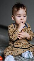 Adorable toddler wearing brown clothes sitting on the carpet in the room. Little baby is busy playing with a cord. Blurred backdrop. Vertical video