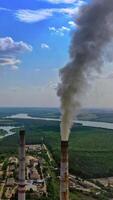 Dirty smoke from industrial pipe. Manufacturing with pipes on nature background with green fields and river. Pollution of environment. Vertical video