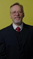 Portrait of happy mature man with apple. Smiling old businessman in costume playing with green apple on the yellow background. Vertical video