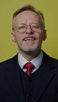 Portrait of smiling businessman on yellow background. Mature man in costume with tie talking and looking on camera. Vertical video