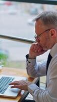 Senior businessman is working on computer in front of the window with city view. of working process in company. Vertical video