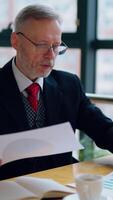 Thoughtful businessman is reading important business papers, in front of the window with city view. of business process. Vertical video