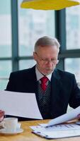 uomo d'affari è lettura un' stampato rapporto o documento mentre seduta a il tavolo, Lavorando su carta opera con il computer portatile a il tavolo. uomo guardare a documenti. attività commerciale . verticale video