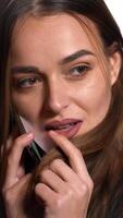Flirty woman talking on the phone and smiling on a white background in the studio. Close-up. Vertical video
