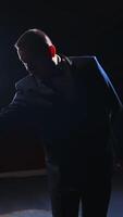 Male actor performing in the theater. Funny man putting on white hat and began dancing on stage in dark light. View from the stage. Vertical video