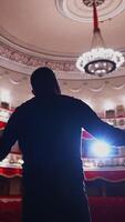 Actor in front of empty theatre hall. Man is standing on stage and talking with gestures before the performance. Vertical video