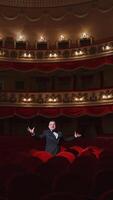Actor among red seats in empty concert hall. Man in suit standing in beautiful large empty auditorium and talking something. Lockdown in the world. Vertical video