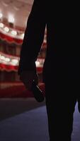 Unrecognizable man in suit on stage. Silhouette of a singer man holding a microphone on the background of empty theater hall. Vertical video