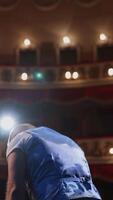 Actor on theater scene with his back to the camera. Man on stage bowing and actively gestures with his hands. Back view. Vertical video